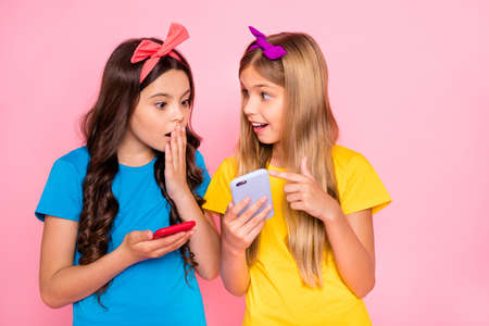 Portrait of impressed girls wear headbands long hairstyle trendy stylish hairstyle, t-shirt hold hand device isolated over pink backgroundの写真素材