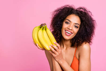 Close up photo beautiful funny she her dark bronze skin body model lady hold hands arms exotic fruit bananas toothy beaming smile fresh food eat wear swimming orange suit isolated pink backgroundの写真素材