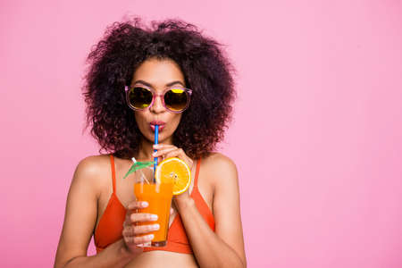 Close up photo beautiful she her dark skin model lady raise hands arms try non sweet diet exotic orange beverage straw mouth cafe bar wear sun specs swimming orange suit isolated pink backgroundの写真素材