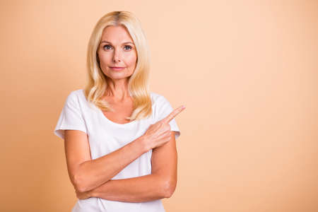 Photo of middle age lady hand indicate empty space self-confident manager wear white casual t-shirt isolated pastel beige backgroundの写真素材