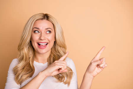 Close-up portrait of her she nice-looking lovely winsome attractive confident cheerful wavy-haired lady pointing two forefingers aside promotion sale discount isolated over beige pastel backgroundの写真素材