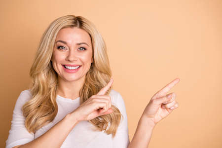 Close-up portrait of her she nice-looking lovely winsome attractive cheerful cheery wavy-haired lady pointing two forefingers aside promotion solution isolated over beige pastel backgroundの写真素材