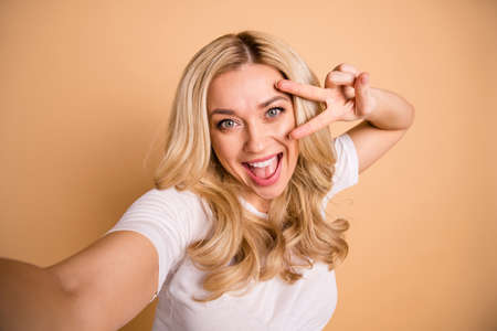 Portrait of charming nice lady make v-signs photos laughter have weekend isolated beige backgroundの写真素材