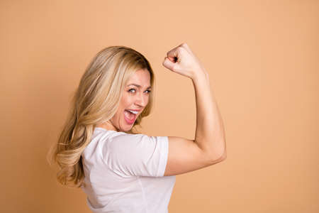 Close-up profile side view portrait of her she nice-looking lovely attractive cheerful cheery ecstatic satisfied wavy-haired lady showing muscles isolated over beige pastel backgroundの写真素材