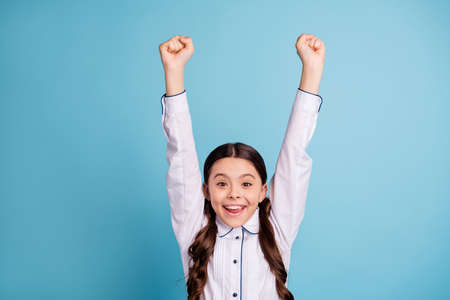Close up of excited child raise fists shout yeah wear white blouse isolated over blue backgroundの写真素材