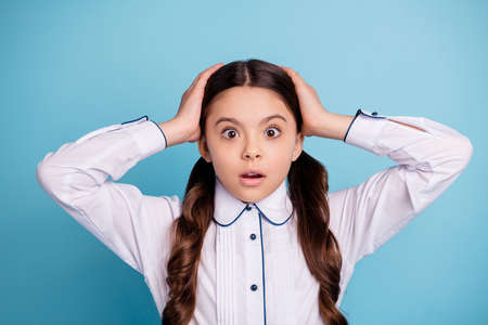 Close up photo of frightened kid hear horrible terrible news touch palms hands head wear white blouse isolated over blue backgroundの写真素材