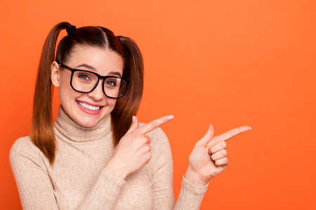 Portrait excited youngster direct present advertise choose novelty tip attention pigtail ponytail promoter indicate ad beautiful trendy eyewear eyeglasses stylish turtleneck isolated orange backgroundの写真素材