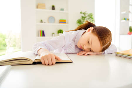 Portrait of sad upset kid little person lie desk close eyes touch printed book sit interior class...