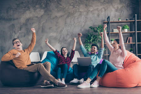 Nice attractive cheerful glad confident guy company specialist development manager employee sitting on bag chairs rising hands up attainment at industrial wooden loft interior workplace workstationの写真素材