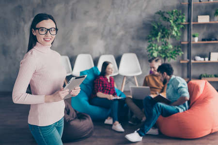 Nice attractive cheerful lady junior specialist financier holding in hands ebook collaboration management sitting on bag chair at industrial wooden loft interior workplace workstationの写真素材