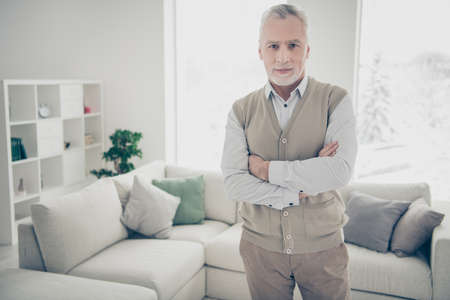 Close up photo amazing manager he him his aged man arms crossed bossy chief look self-confident wear white shirt waistcoat pants stand near cozy comfort divan bright flat house living room indoorsの写真素材
