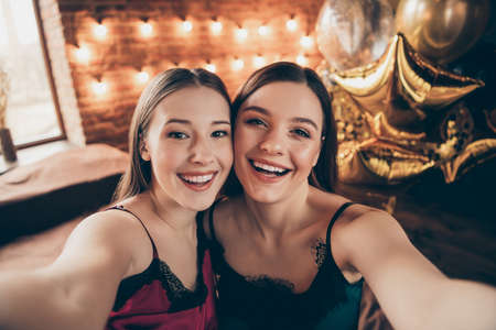 Close up photo amazing beautiful two she her fancy cute chic ladies make take selfies toothy sit bed linen sheets fellows buddies wear sleep costumes girls day night theme party house room indoorsの写真素材