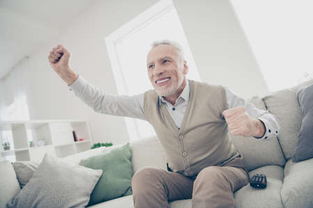Close up photo amazing funky he him his aged man observe sports match, game achievement arms hands raised air wear white shirt waistcoat pants sit comfort bright flat house living room indoorsの写真素材