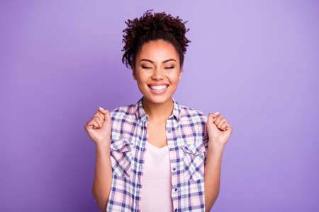 Close-up portrait of nice charming cute attractive lovely lovable cheerful cheery optimistic wavy-haired girl in checked shirt holding fists closed eyes isolated over violet purple pastel backgroundの写真素材