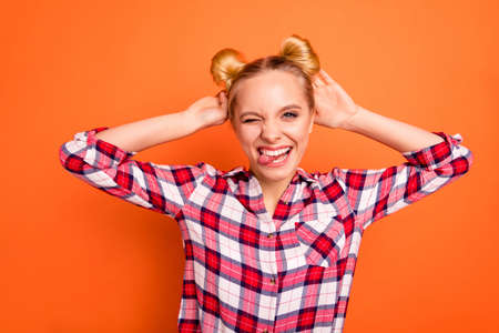 Close up photo beautiful pretty she her nice lady arms hands touch hair buns tongue out mouth blink eye childish mischief person wear casual checkered plaid pink shirt isolated orange backgroundの写真素材