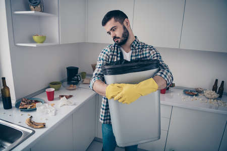 Portrait of attractive serious focused sad bored tired bearded guy wearing checked shirt doing domestic mess chaos in modern light white interior style kitchen indoorsの写真素材