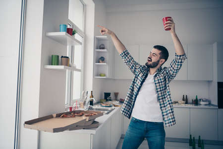 Portrait of nice attractive careless carefree cheerful cheery bearded guy wearing checked shirt having fun disco time vacation in modern light white interior style kitchen indoorsの写真素材