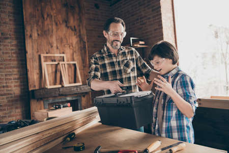 Portrait of two nice person cheerful cheery glad successful woodworkers master handyman dad giving new toolkit to son production industry at modern loft industrial brick interiorの写真素材