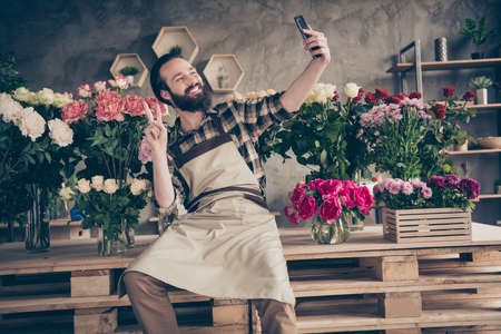 Portrait of his he nice attractive cheerful cheery positive guy gardener sitting making selfie showing v-sign at modern industrial loft concrete style salon indoorsの写真素材