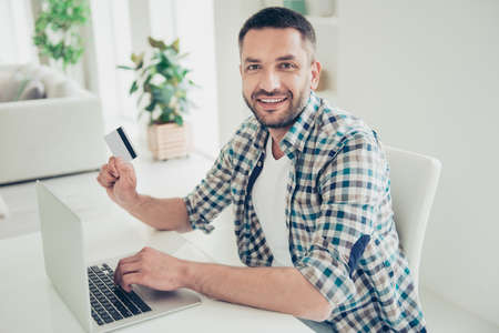 Portrait of imposing positive man work worker hold hand have salary save savings he his fun sit divan use user netbook big apartment room test type plaid shirtの写真素材