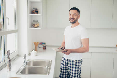 Close up photo attractive he him his homey guy arms hands clean plate glad be home help wife girlfriend duties chores stand cheerful positive white t-shirt checkered pants bright kitchen room indoorsの写真素材