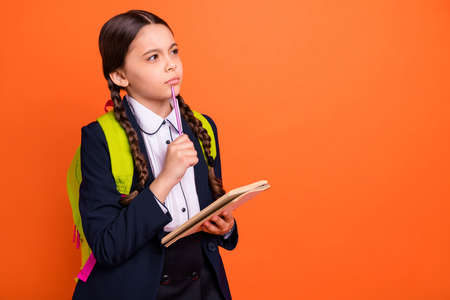 Close up side profile photo beautiful she her little lady hands arms pen chin notebook note information teacher ponder wear formalwear shirt blazer school form bag isolated bright orange backgroundの写真素材