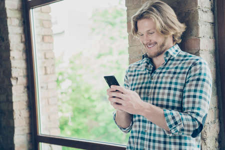 Profile side photo of cheerful man holding device looking reading news wearing checkered plaid shirt standing in interiorの写真素材