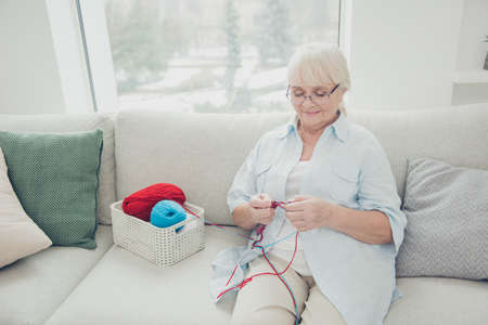 Portrait of her she single nice attractive focused concentrated cheerful peaceful calm granny sitting on divan having rest relax spending weekend knitting in light white interior living-room houseの写真素材