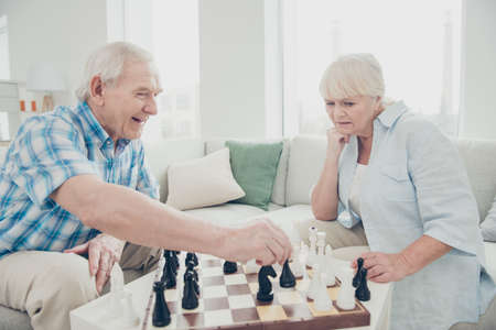 Profile side view portrait of her she his he two nice attractive bewildered concentrated focused people playing chess creating move strategy win winner in light white interior living-room houseの写真素材