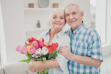 Photo of two adorable aged people hugging pair anniversary holiday surprise big red tulips bunch...