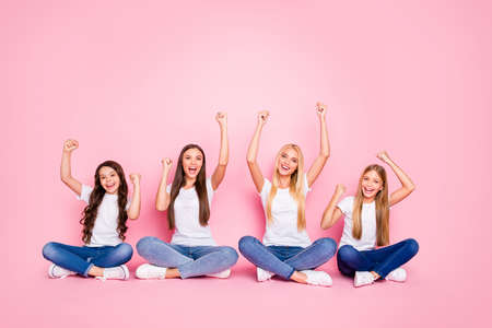 Nice attractive lovely cheerful cheery glad positive confident girls sitting on floor crossed legs celebrating good news rising hands up rejoice solution isolated over pink pastel backgroundの写真素材