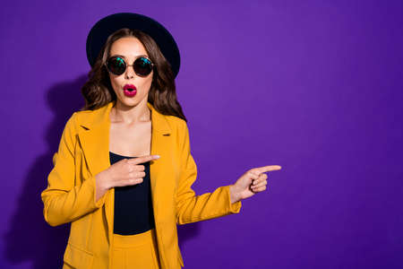 Excited lady with open mouth indicating fingers empty space wear specs yellow costume isolated...