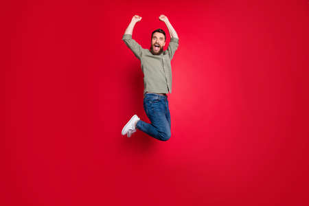 Full length body size photo of rejoicing happy man jumping with victory while isolated with red backgroundの写真素材