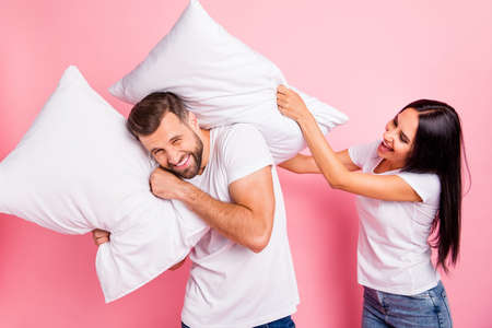 Photo of crazy casual couple destroying each other with pillow while isolated with pink backgroundの写真素材