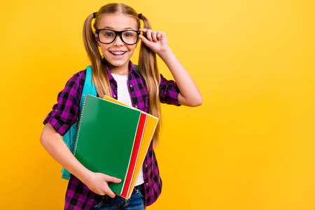 Close up photo of little lady pupil hold copybooks pretty ponytails wear specs checkered shirt isolated yellow backgroundの写真素材