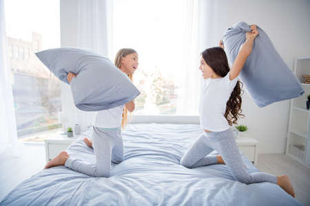 Profile side photo of cute adorable children have competition hold hand pillows scream sit bed room interior indoorsの写真素材