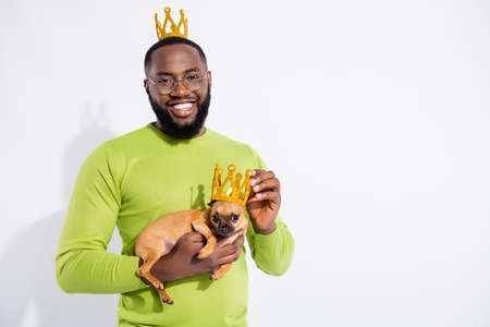 Portraiit of cheerful guy holding his toy terrier looking wearing gold tiara diadem eyewear...