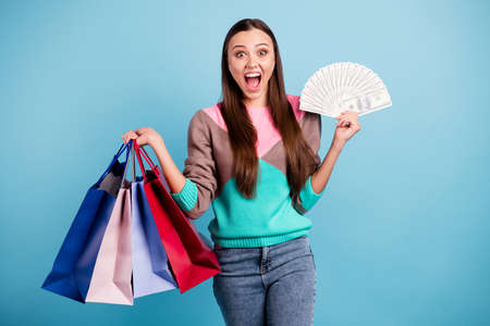 Photo of astonished screaming wow omg funny girl holding several bags in hands showing pile of american banknotes currency isolated vivid backgroundの写真素材