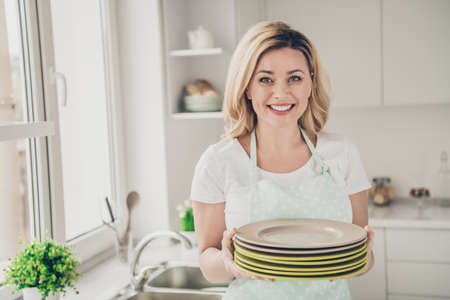 Close-up portrait of her she nice attractive lovely cheerful cheery content wavy-haired girl holding in hands plates cleanup cozy comfort done in light white interior kitchen indoorsの写真素材