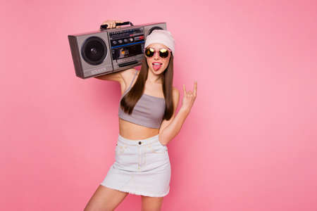 Portrait of beautiful trendy stylish girl making horns holding boombox screaming grimacing wearing...