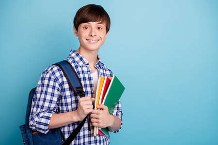 Portrait of charming college student holding note books looking wearing checked shirt isolated over blue backgroundの写真素材