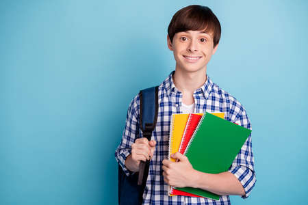 Portrait of lovely student holding note books wearing checked shirt isolated over blue backgroundの写真素材