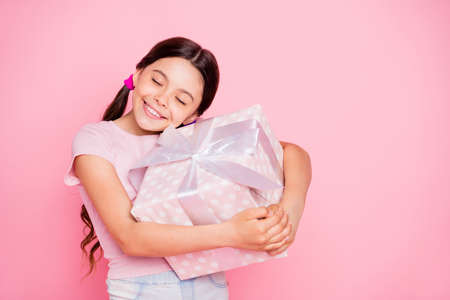 Portrait of lovely child holding giftbox hugging closing eyes wear white t-shirt isolated over pink backgroundの写真素材