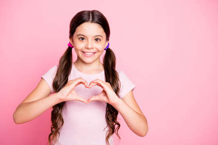 Portrait of cheerful kid showing heart make from fingers smile wear white t-shirt isolated over pink...