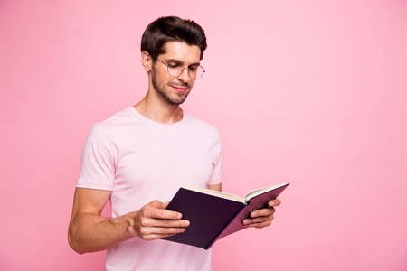 Portrait of his he nice attractive lovely diligent peaceful focused concentrated intelligent guy holding in hands reading book library lesson preparing exam isolated over pink pastel backgroundの写真素材