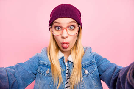 Photo of cute playful amazed girl disliking her friends decision and showing him her tongue while isolated with pink backgroundの写真素材