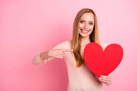 Photo of beautiful lady hold hand big paper heart figure invitation prom indicate finger wear pastel pullover isolated pink backgroundの写真素材