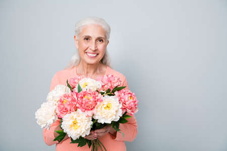 Close up photo of pretty cute sweet kind friendly sincere lady holding nice flowers in hands isolated grey backgroundの写真素材
