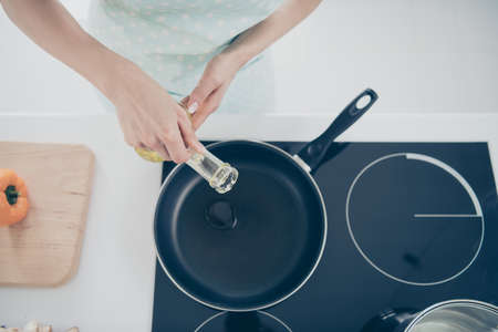 Cropped top above and hing angle view photo of woman pouring sunflower oil into skillet to begin frying vegetablesの写真素材