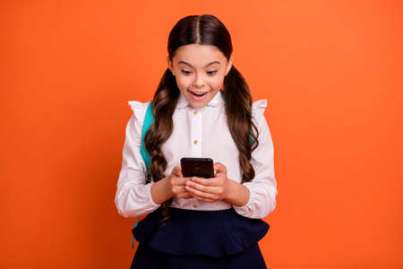 Portrait funny funky impressed little child hold hand modern technology chilling chatting wow omg unbelievable news shirt blouse skirt dress stylish tails ponytails pigtails isolated orange backgroundの写真素材